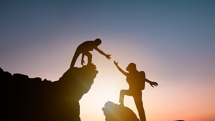 Silhouette of climbers with the sun in background, one is reaching out to the other
