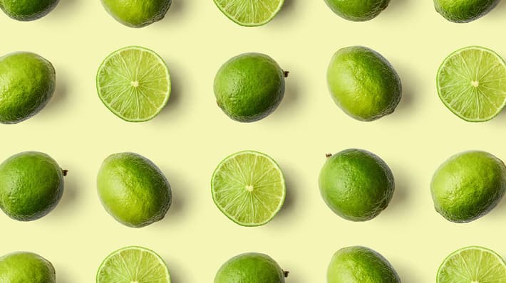 An image of whole limes and limes cut in half and arranged on a light yellow background