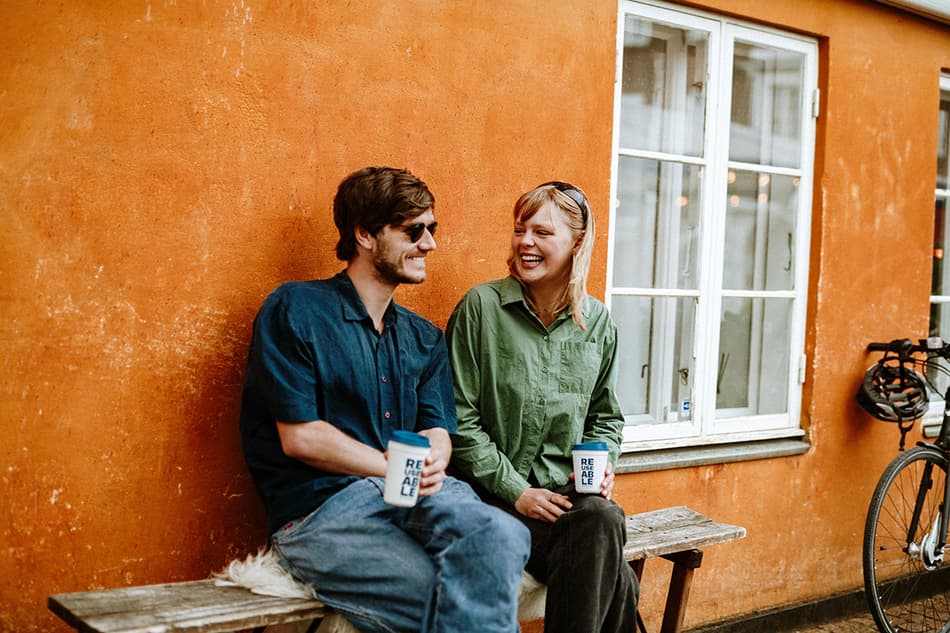 man and woman sitting on bench in Aarhus, each holding a REUSEABLE cup 