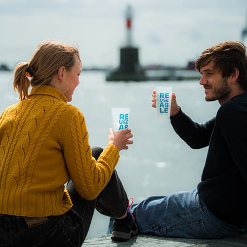 Young couple sitting by the city harbor with reusable cups