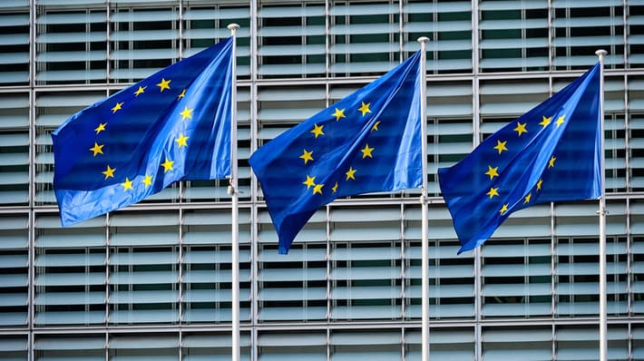 three EU flags flying against background of modern office building