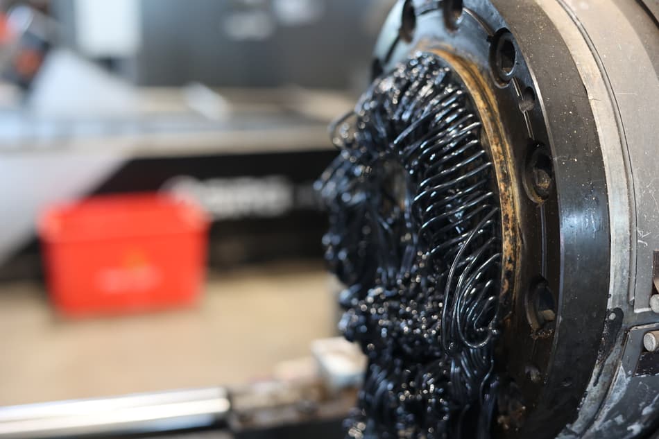 Black molten plastic squeezing out of a machine like spaghetti