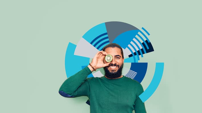 Man with green sweater holding a slice of kiwi fruit up to his eye