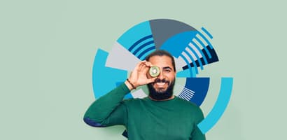 Man with green sweater holding a slice of kiwi fruit up to his eye
