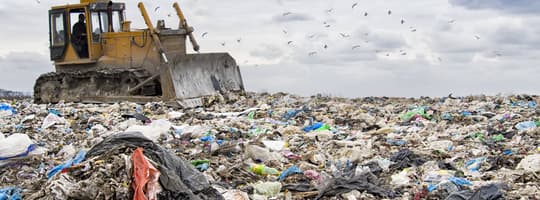 Landfill compactor gathering trash at landfill site