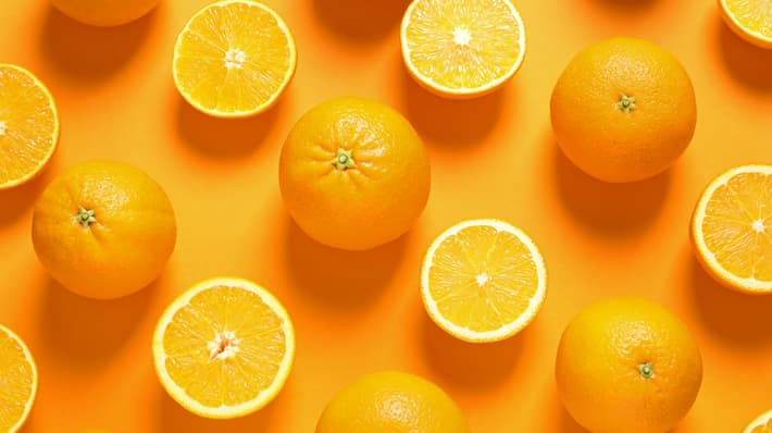 An image of oranges both whole and cut in half laying flat on an orange background
