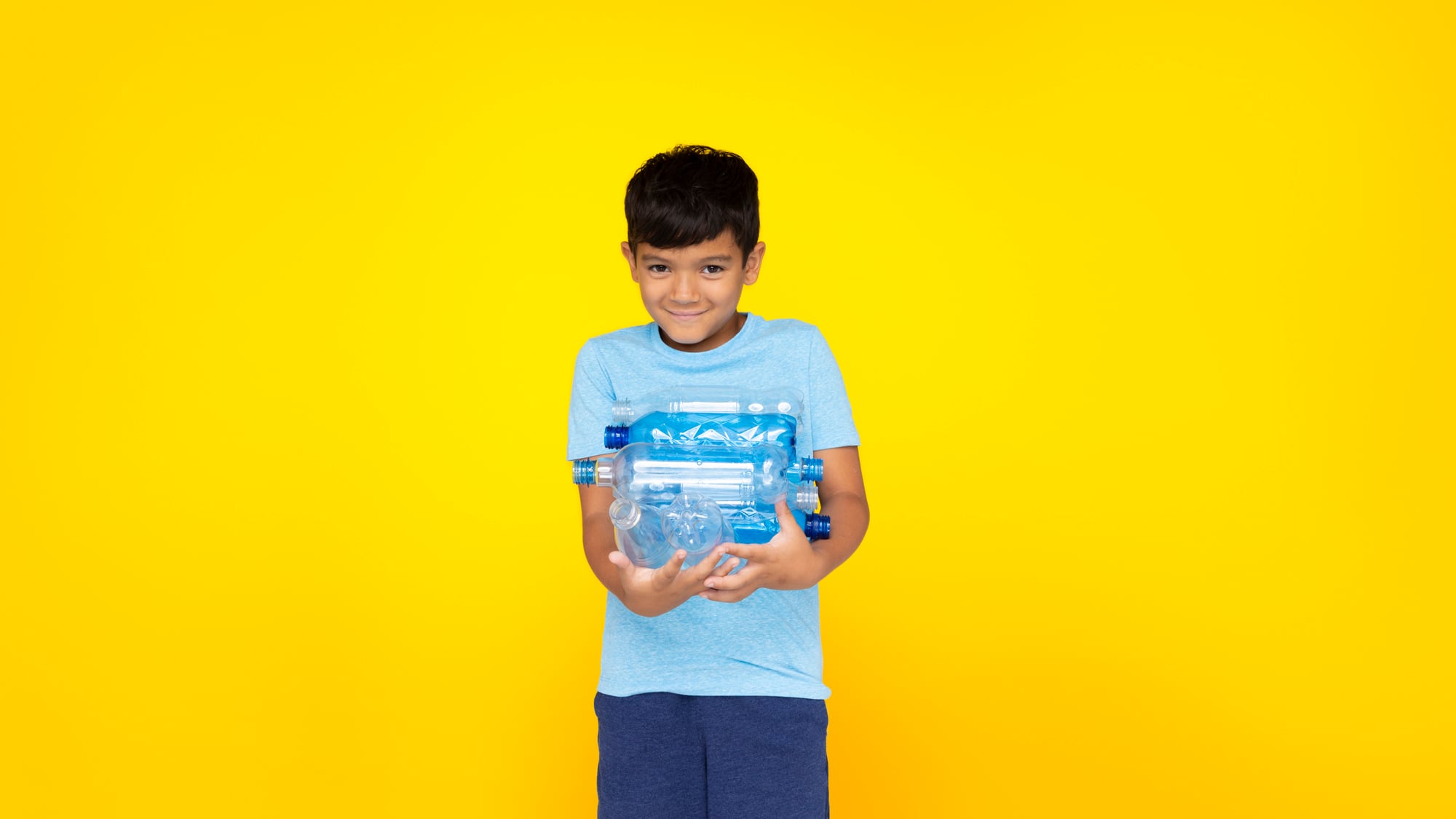 Boy yellow bckg holding PET bottles