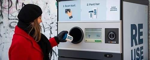 Woman in red coat and black hat returning reusable cup at TOMRA Reuse machine