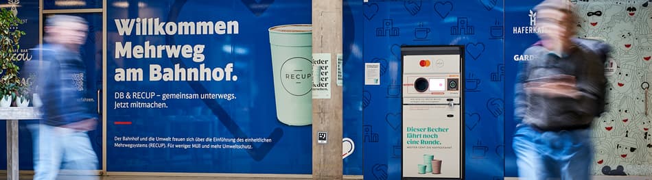Blurred profiles of two people walking by TOMRA Recup return machine installation at Freiburg central train station