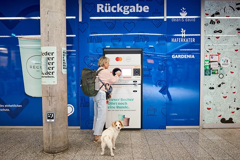 Woman with her dog returning reusable RECUP at TOMRA return machine at Freiburg central train station