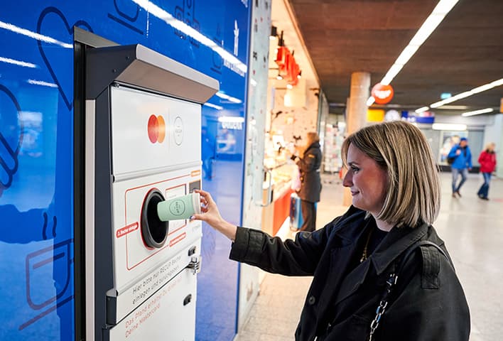 Woman returning a RECUP reusable cup at TOMRA return station at Freiburg central train station in Germany