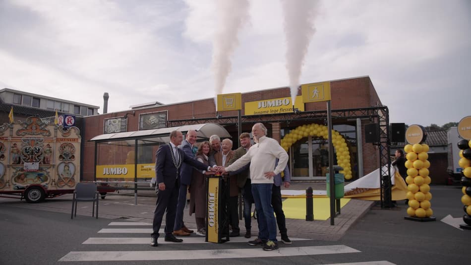 A group of people celebrating outside a supermarket with smoke and balloons.