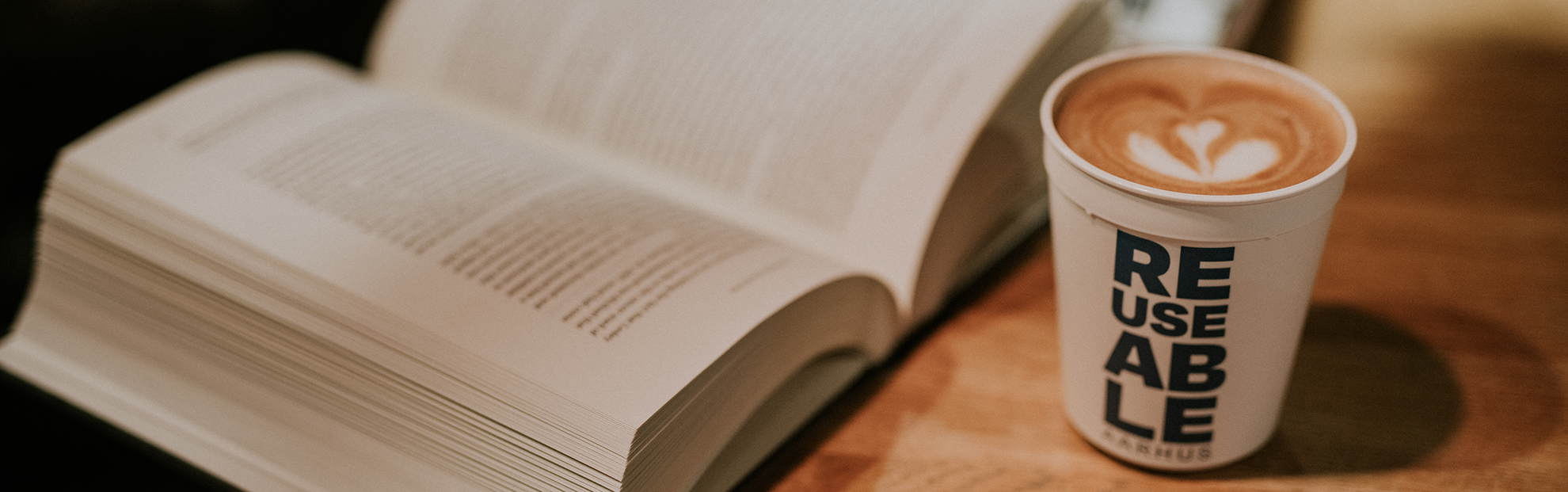 A cup of takeaway coffee in a REUSEABLE cup next to an open book